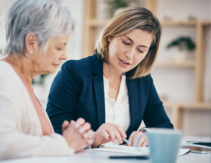 Senior woman and sales agent sitting at a table going over plan paperwork
