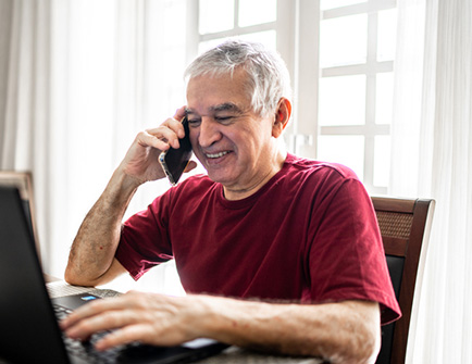 Senior man on the phone in front of a laptop.